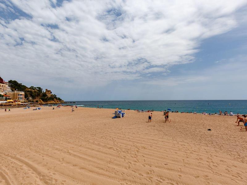 Amplia playa de arena con pocas personas, al fondo el mar y cielo nublado.