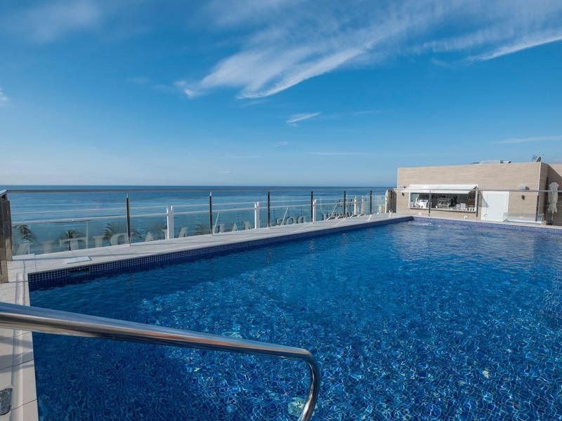 Piscina infinita moderna en una azotea con vista al mar bajo un cielo azul.