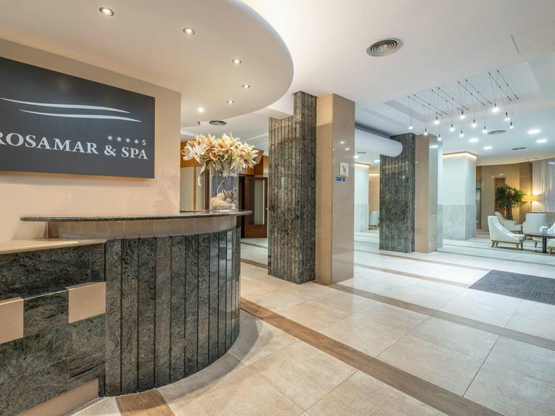 Lobby de hotel luminosa con mostrador de recepción, área de descanso lateral e iluminación moderna.