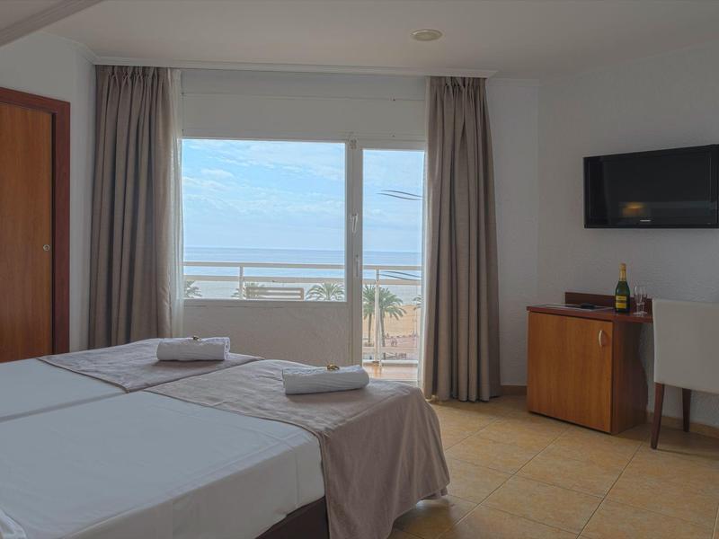 Habitación de hotel moderna con cama doble, balcón con vista al mar y TV en la pared.
