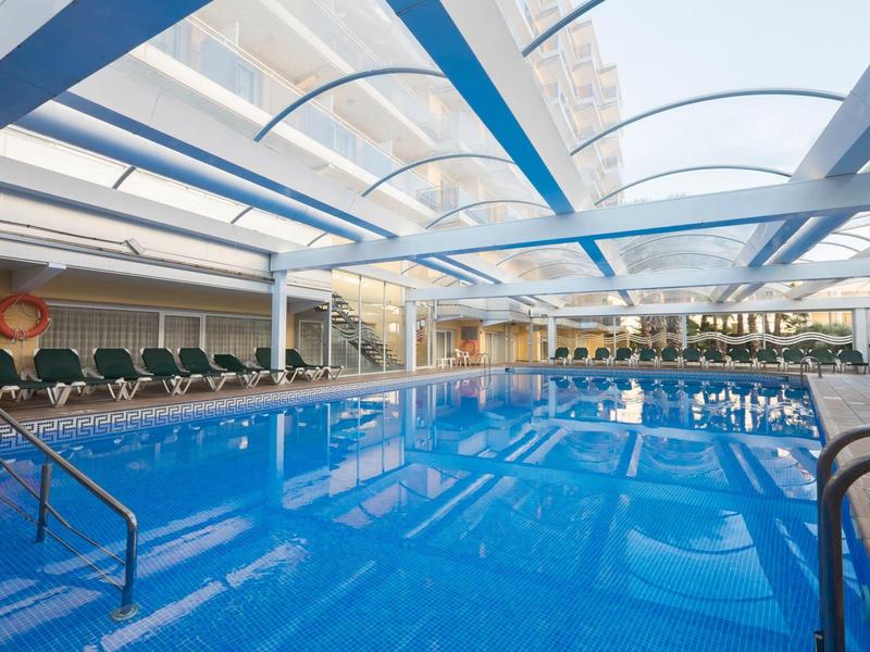 Zadaszony basen kryty z niebieską wodą i rzędami leżaków.