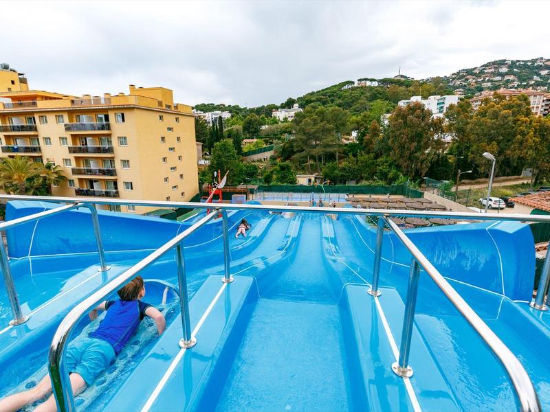 Widok na szerokie niebieskie zjeżdżalnie wodne z poręczami schodów w strefie basenu hotelowego.