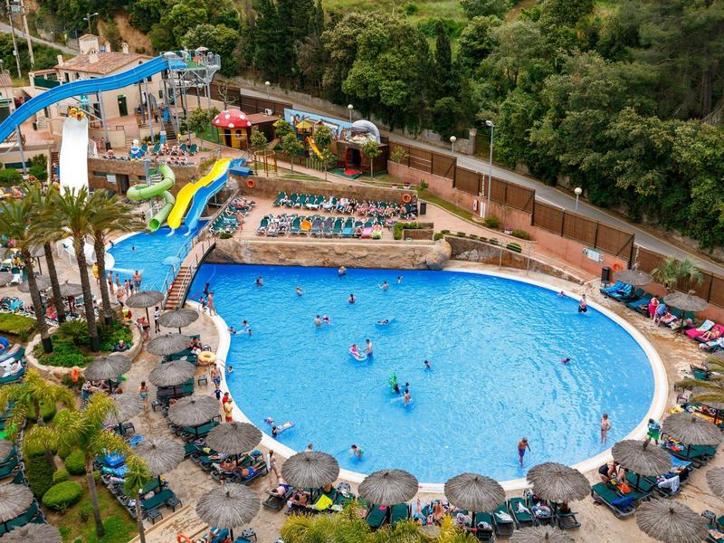 Park rozrywki z dużym basenem, zjeżdżalniami i leżakami otoczony drzewami.