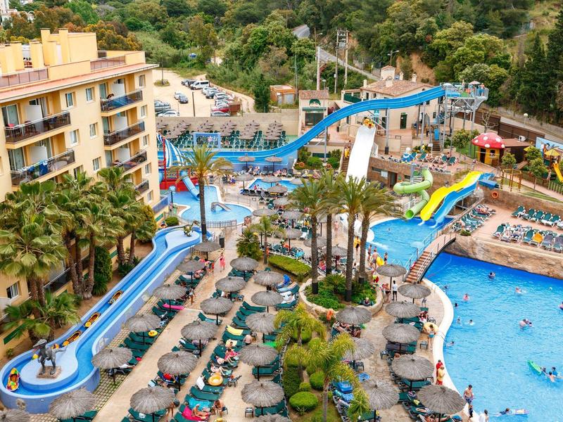 Park wodny z kolorowymi zjeżdżalniami i basenem otoczonym leżakami.