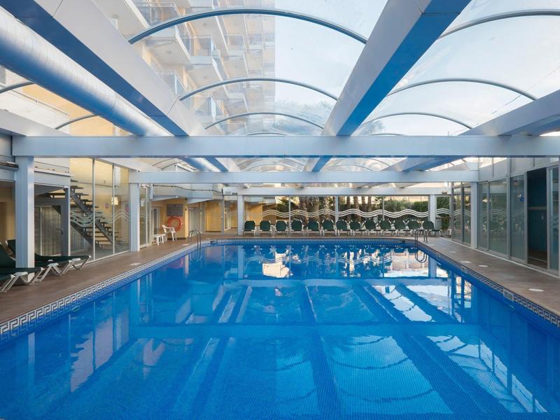 Podgrzewany basen kryty z szklanym dachem i leżakami w nowoczesnym hotelu.