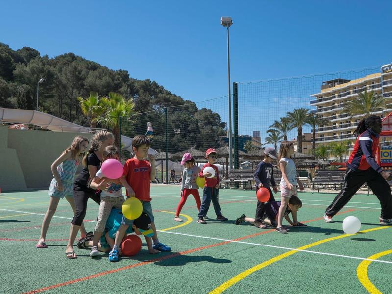 Dzieci bawiące się na zewnątrz na boisku sportowym przy słonecznej pogodzie.
