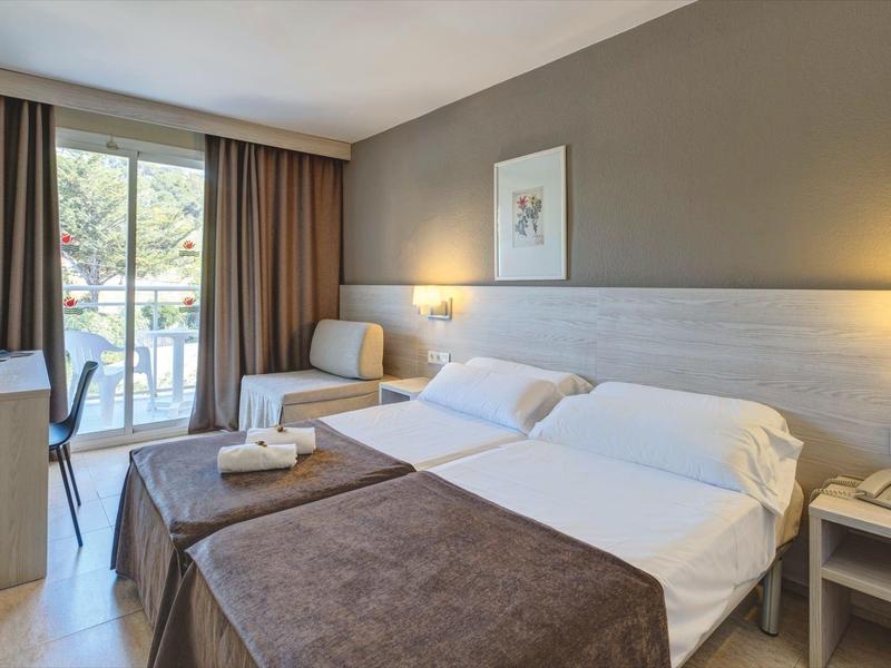 Przytulny pokój hotelowy z łóżkiem podwójnym, balkonem i widokiem na zieleń.