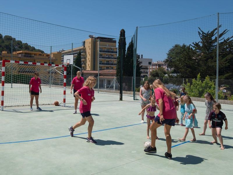 Dzieci grają w piłkę nożną z opiekunami na zewnątrz w słoneczny dzień.