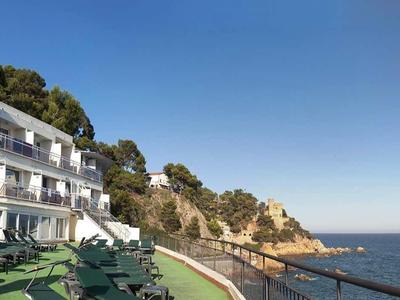 Terrasse d'hôtel avec chaises longues, vue sur la mer et la côte rocheuse sous un ciel dégagé