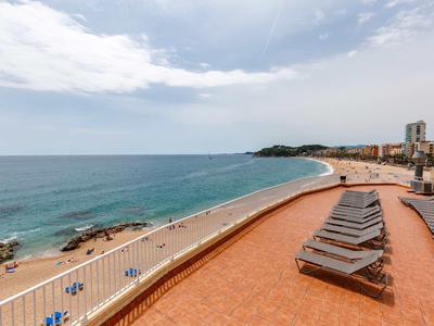 Terrasse ensoleillée avec transats offrant une vue sur une large plage de sable et la mer.