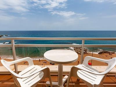 Balcon avec deux chaises blanches et une petite table ronde avec vue sur la mer sous un ciel nuageux.