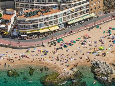 Plage avec des personnes et des rochers devant un grand bâtiment hôtelier au bord de la mer