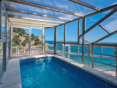 Piscine intérieure avec toit en verre offrant une vue sur la mer et la côte au soleil.
