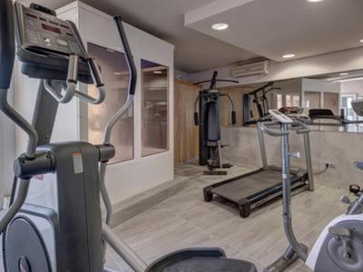 Gimnasio moderno con cinta de correr, elíptica y vista al mar a través de grandes ventanales.