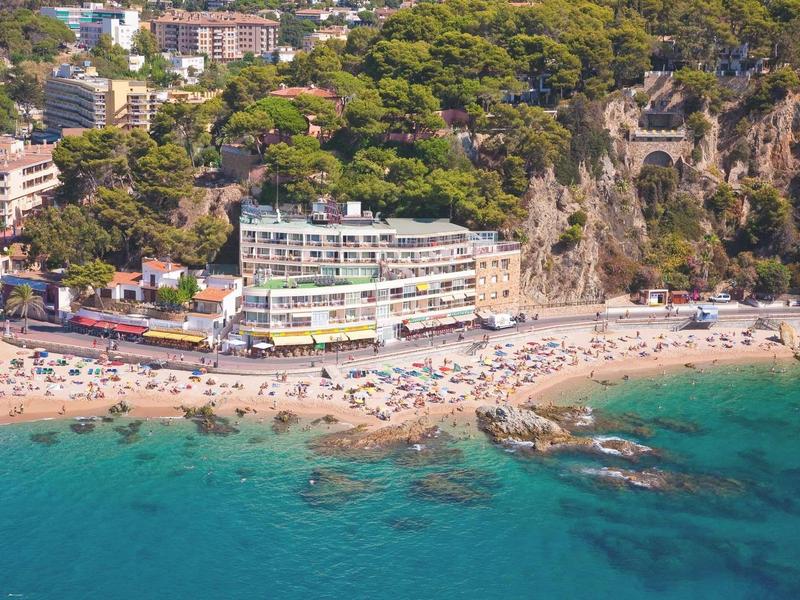 Hôtel en bord de mer sur une côte rocheuse avec une colline boisée à proximité.