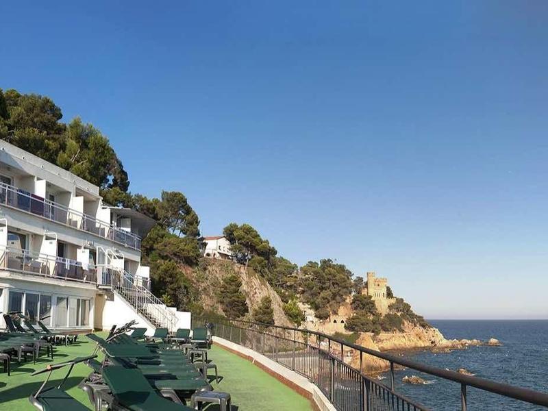 Terrasse d'hôtel avec chaises longues, vue sur la mer et la côte rocheuse sous un ciel dégagé