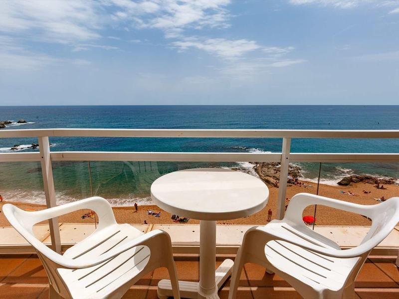 Balcon avec deux chaises blanches et une petite table ronde avec vue sur la mer sous un ciel nuageux.