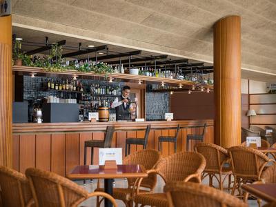 Cozy hotel bar with wicker chairs and wooden counter in a warm, modern setting.