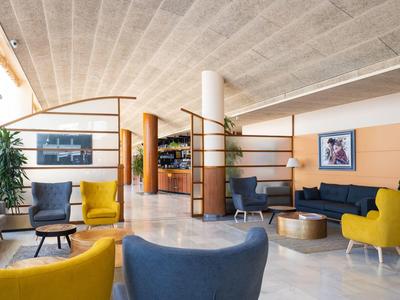 Modern, inviting hotel lounge with colorful armchairs, decorative plants, and elegant marble flooring.