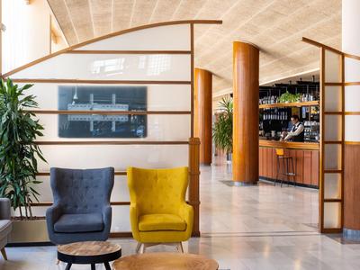 Modern eingerichteter Hotel-Loungebereich mit Sitzgelegenheiten in Gelb und Blau, Pflanzen und Holzakzenten.