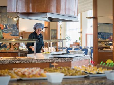 Chef preparing a buffet in bright restaurant kitchen with various dishes.
