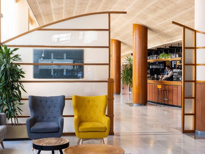 Modern hotel lobby with cozy armchairs, wooden room dividers, and an integrated bar.