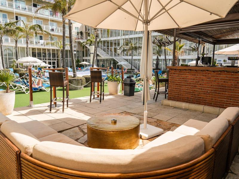 Cozy lounge area with sun umbrella in front of bar and hotel in the background.