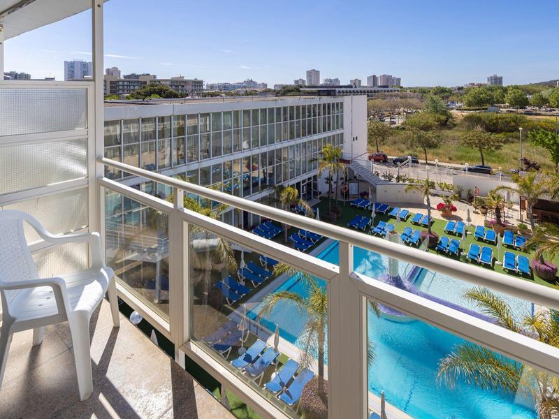 Balcony with chair overlooking hotel pool and garden area under clear sky.