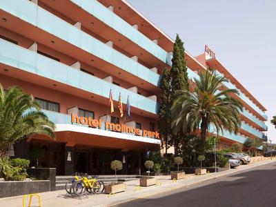 Modern hotel building with large balconies, palm trees, and bicycles at the entrance.