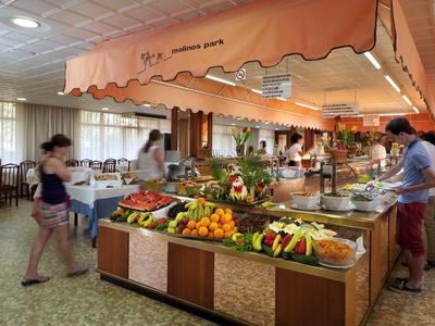 Buffet area in a hotel restaurant with fruits, vegetables, and several guests.