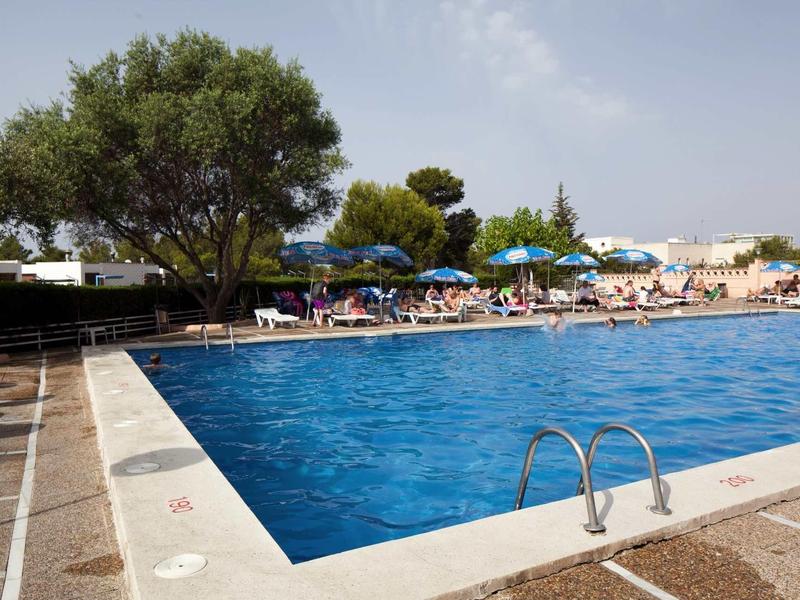 Large outdoor pool with ladders, umbrellas, and lounge chairs on a sunny day.