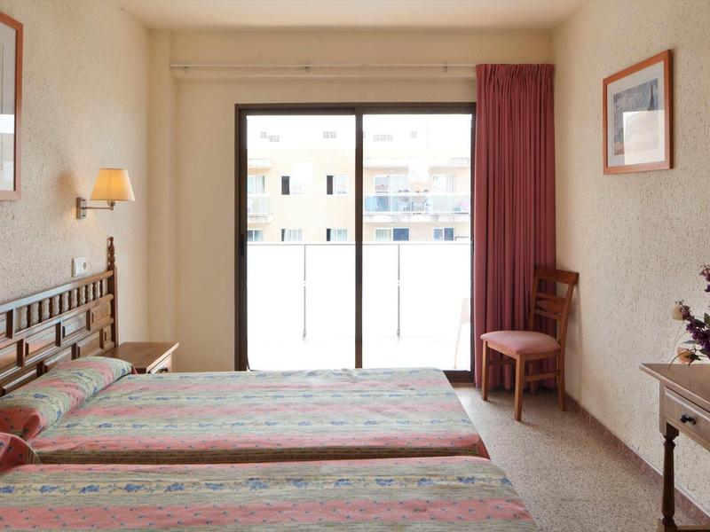 Brightly furnished hotel room with two beds and a window overlooking the balcony.
