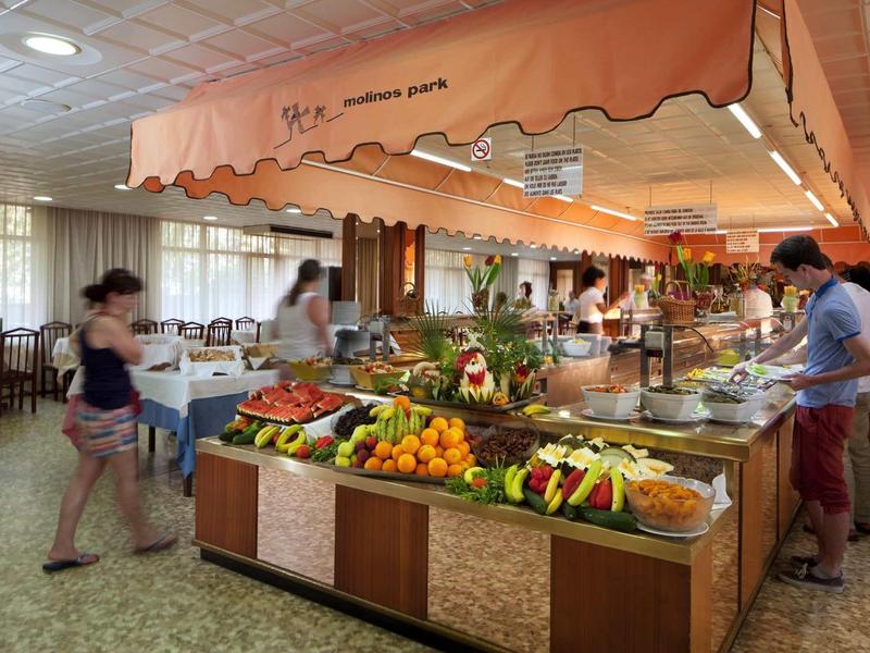 Buffet area in a hotel restaurant with fruits, vegetables, and several guests.