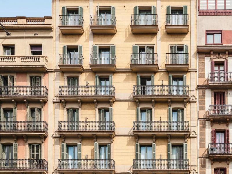 Albergo beige alto con balconi sotto un cielo azzurro limpido.