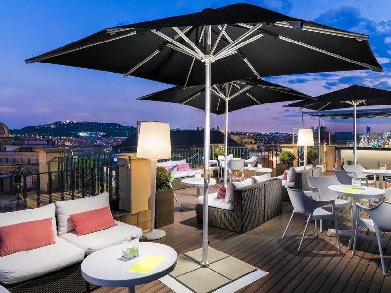Terrazza panoramica con posti a sedere, ombrelloni e vista notturna sulla città, ideale per rilassarsi.