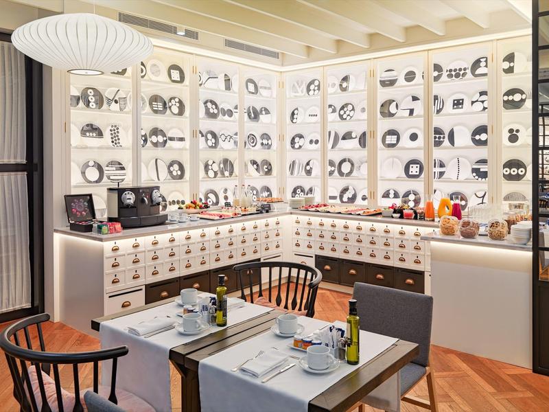 Cucina moderna con mobili bianchi, sedie nere e piatti decorativi a parete in una stanza luminosa.