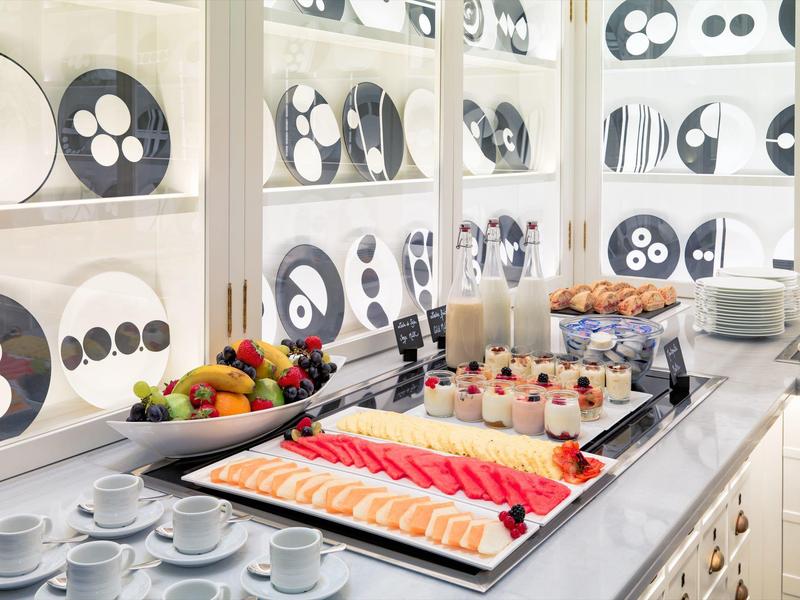 Un buffet per la colazione luminoso con frutta, pasticcini, yogurt e tazze da caffè.