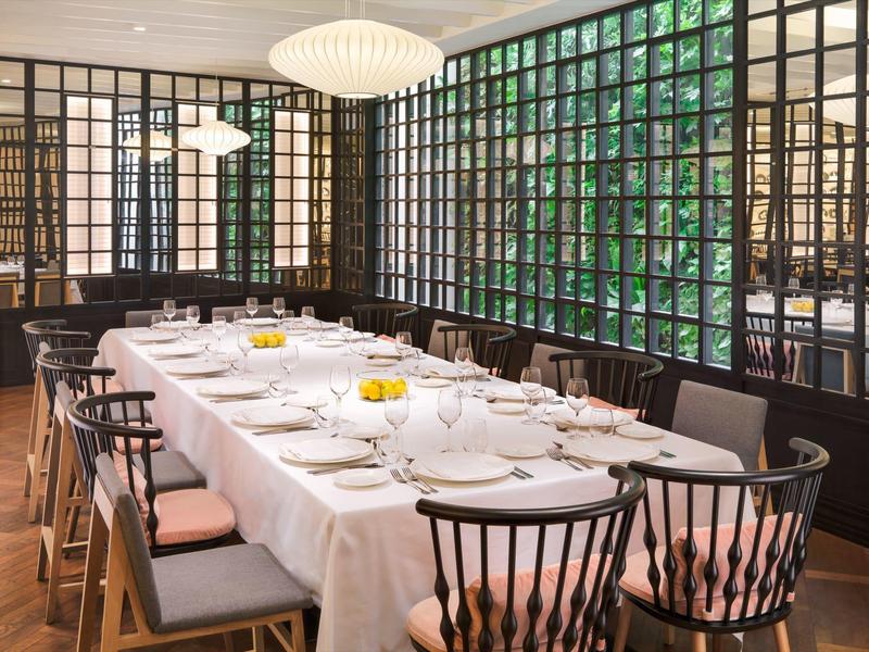 Sala da pranzo elegante con tavolo lungo apparecchiato accanto a grandi finestre a griglia.