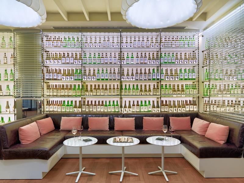 Area lounge moderna con sedute imbottite e scaffali pieni di bottiglie.