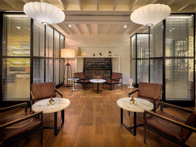 Lounge di hotel elegante con pavimenti in legno, poltrone comode, tavoli rotondi e grandi lampade a soffitto.