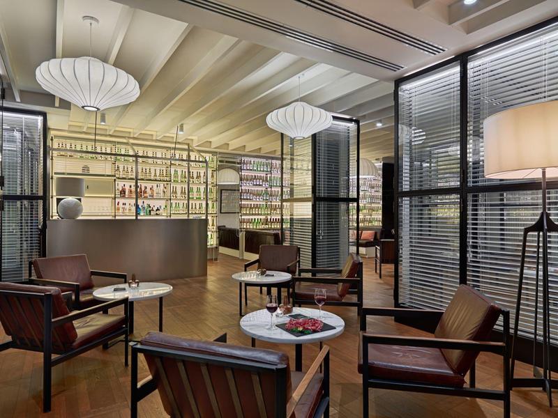 Accogliente lounge dell'hotel con poltrone eleganti, tavoli, banco bar e illuminazione calda.