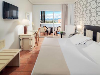 Habitación de hotel luminosa con cama doble, área de estar, decoración en la pared y televisor en la pared.