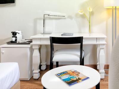 Área de trabajo moderna en hotel con escritorio blanco, silla, lámpara y cafetera en la habitación.