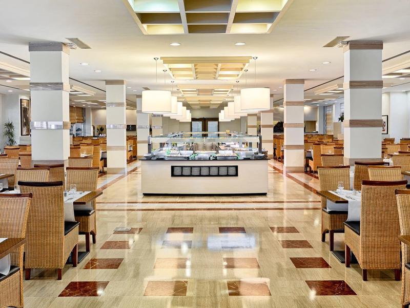 Gran comedor de restaurante de hotel con muchas mesas y sillas de madera y área de buffet.