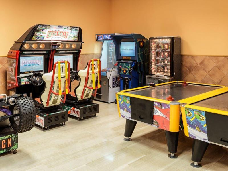 Sala de juegos con máquinas arcade clásicas y mesa de air hockey en habitación con luz cálida