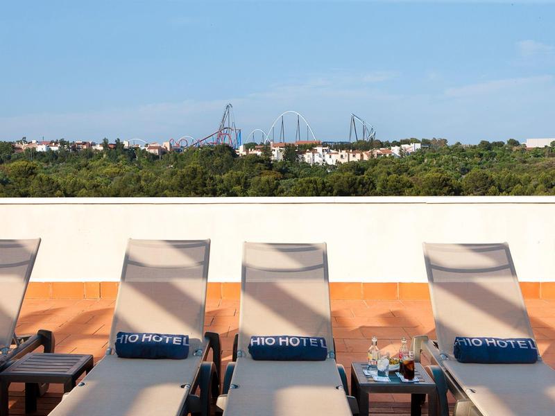 Terraza en la azotea con tumbonas y vista a árboles verdes y ciudad al fondo.