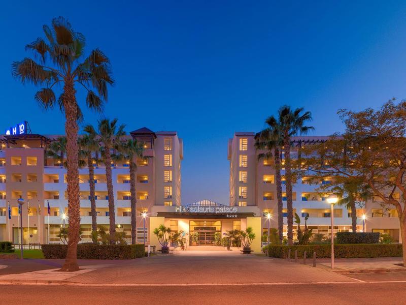 Un edificio de hotel iluminado al anochecer con palmeras y cielo despejado.
