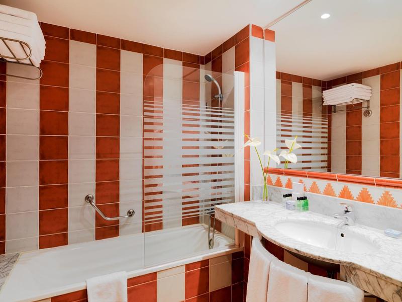 Baño moderno con bañera, ducha, lavabo blanco y azulejos a rayas rojas y blancas.