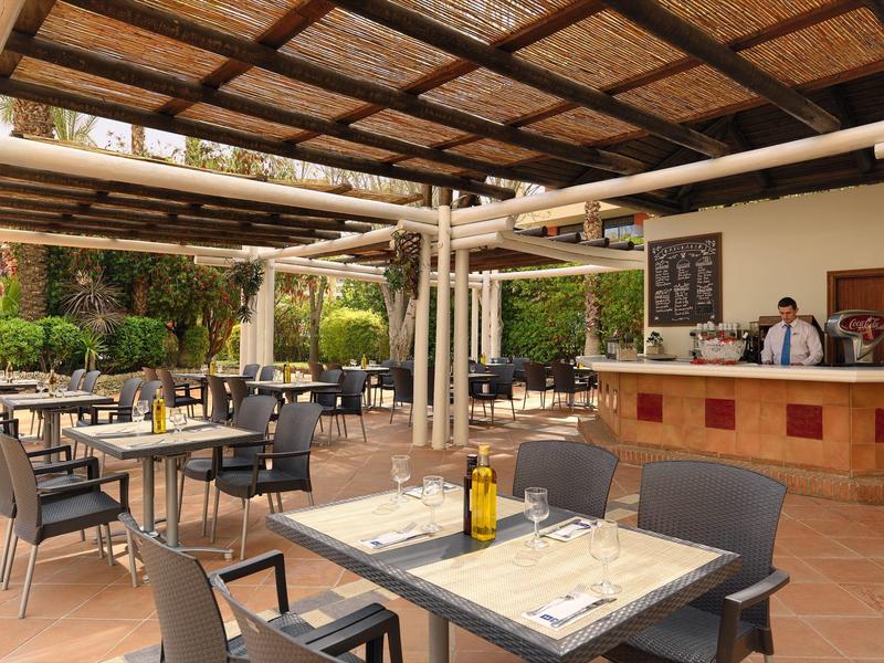 Área exterior de restaurante con mesas preparadas y zona de servicio bajo techo de madera y bambú.