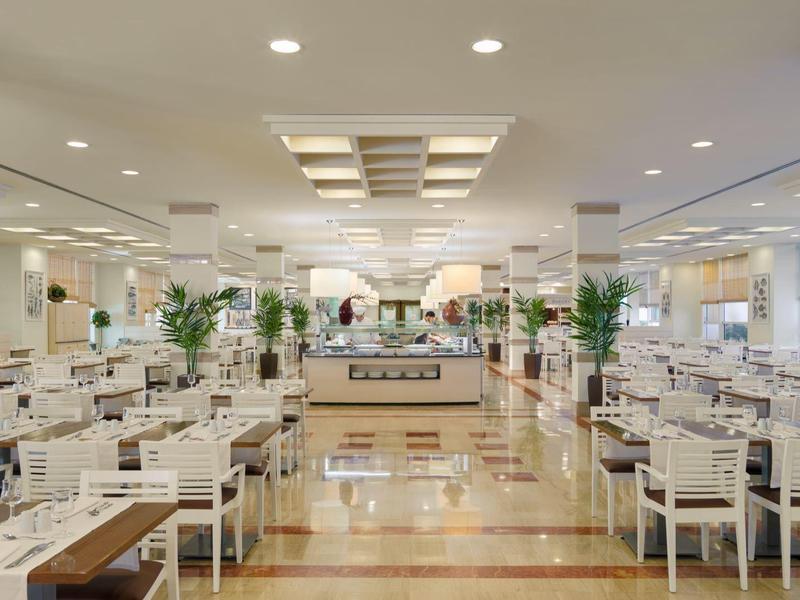 Amplio y luminoso comedor del hotel con mesas y sillas blancas y plantas en macetas.